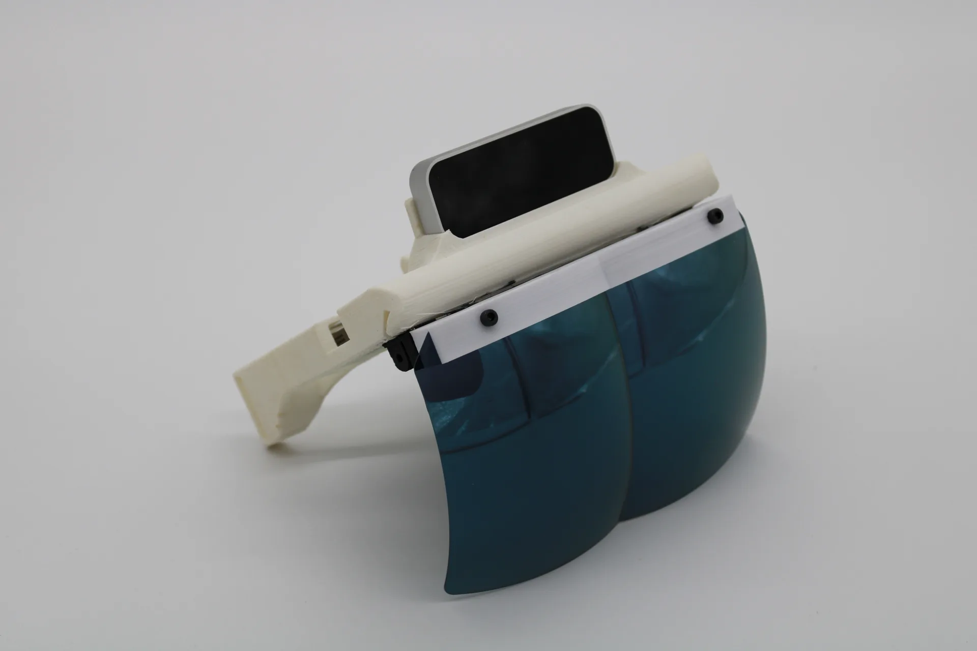 A white 3D-printed headset frame with a dark display slotted in at the top and a curved blue-tinted visor below, on a grey studio background.