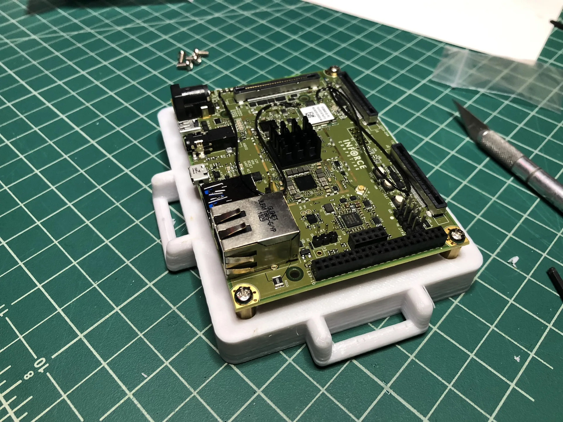 A compute board with a heat sink and network port, seated in a white 3D-printed enclosure with handles, on a green cutting mat.