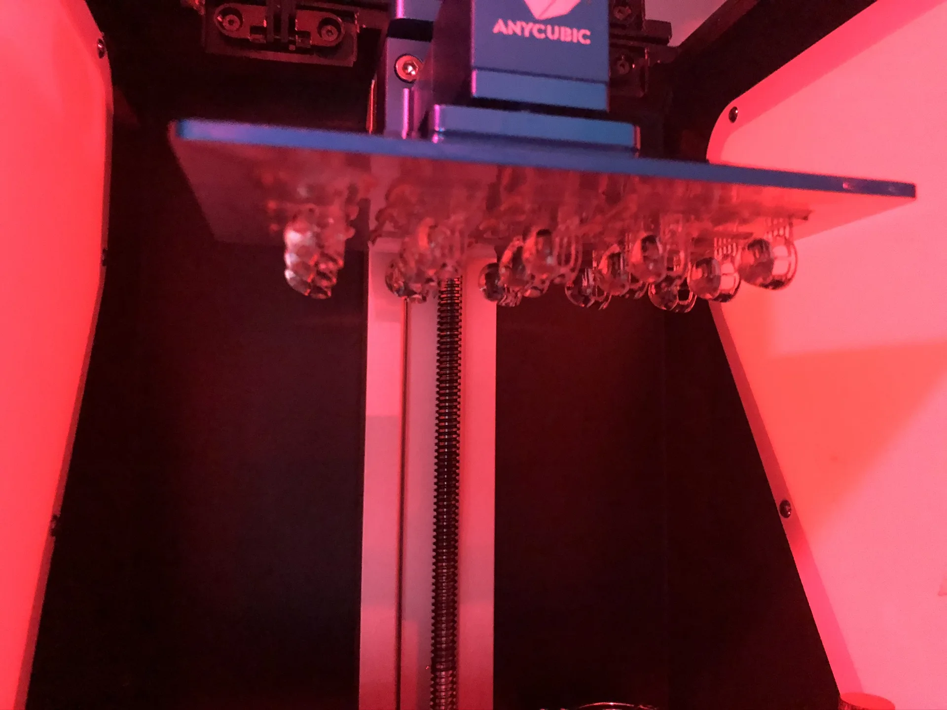 A resin printer's build plate with a row of small clear lens prints hanging from it.
