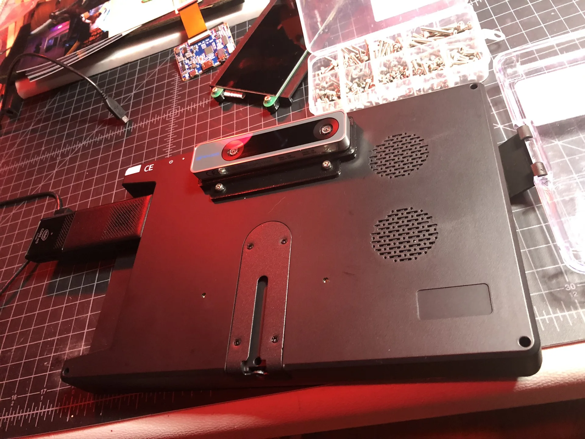 A black tablet-sized display panel with a tracking camera mounted on its back, on a red-lit workbench.