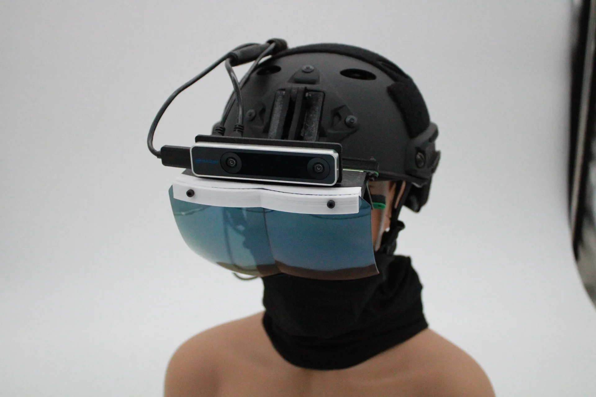 Front three-quarter view of the tactical helmet with the HoloFlect sensor bar and blue-tinted visor lowered over the mannequin's eyes.