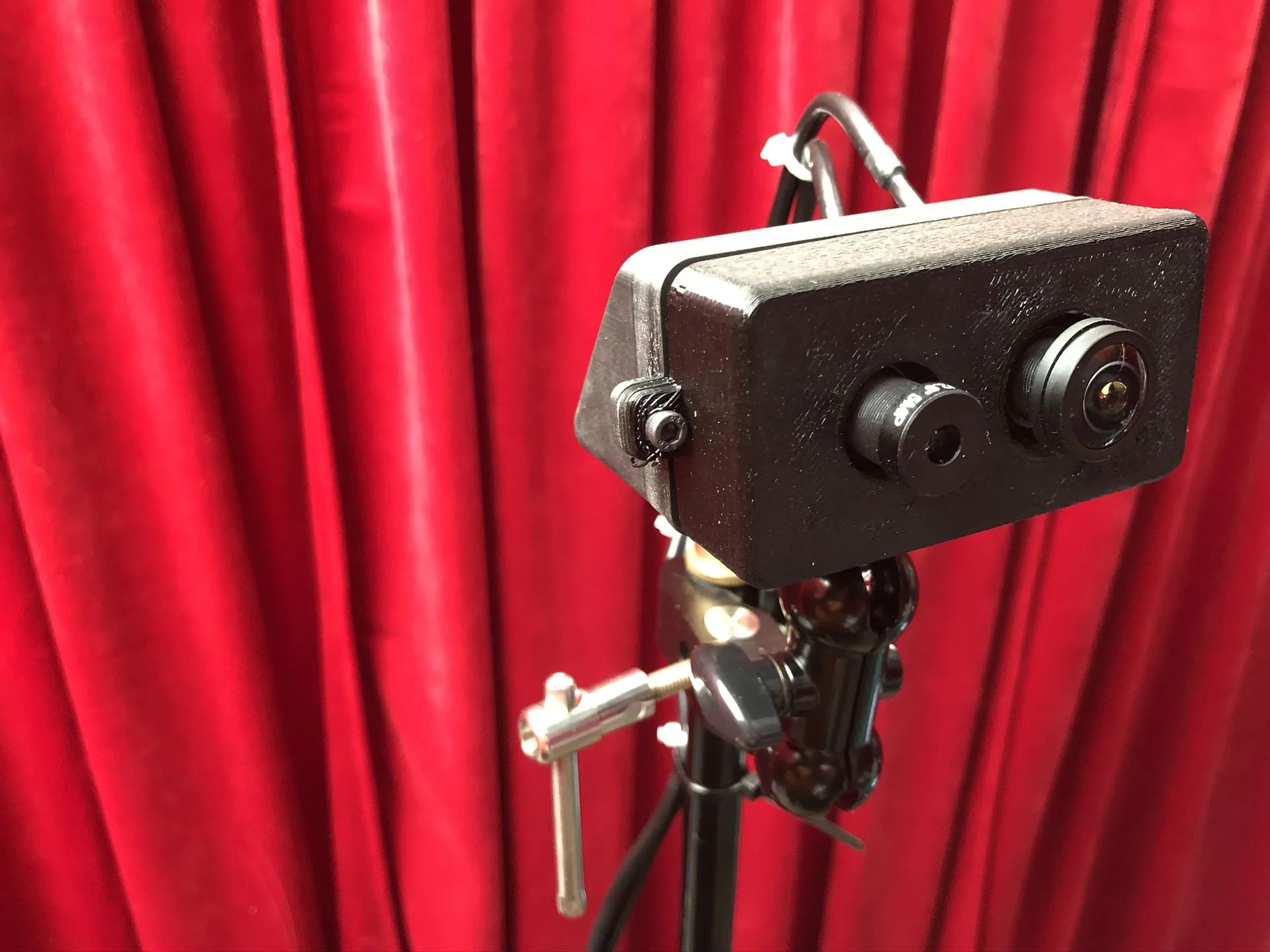 The enclosure on a clamp and ball mount atop a light stand, in front of a red curtain.