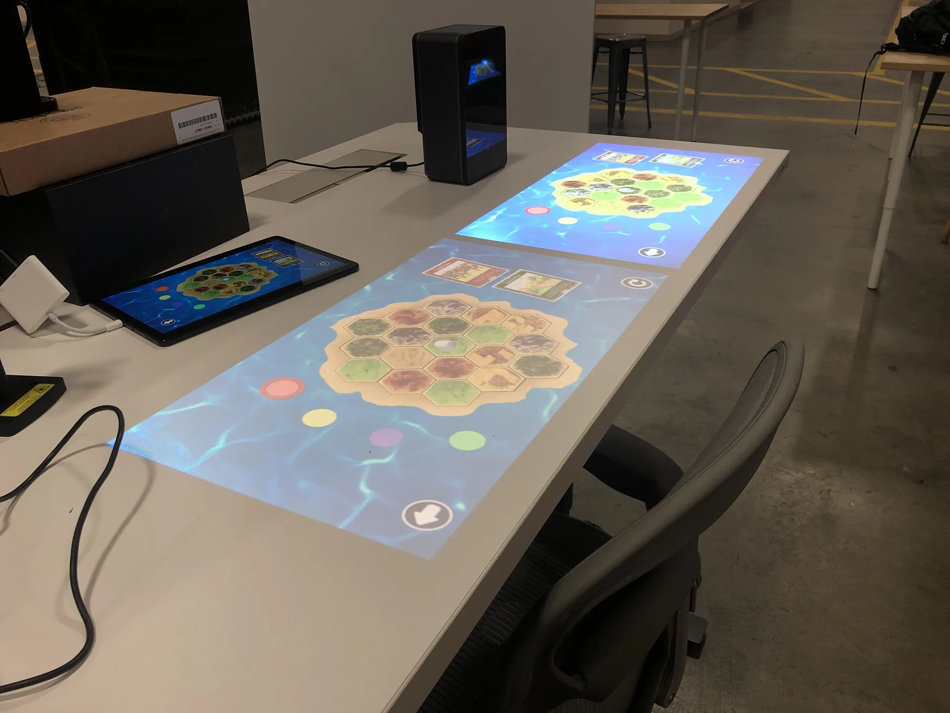 The projected hex-tile board and cards seen from the side of the table, with the projector unit at the back.