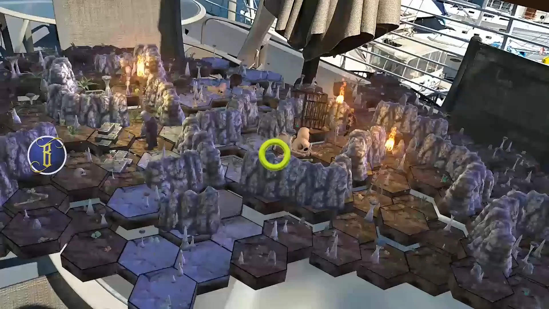 A ring of purple rock walls and hex tiles with a lit fire at the center, rendered on a patio table next to a harbor.