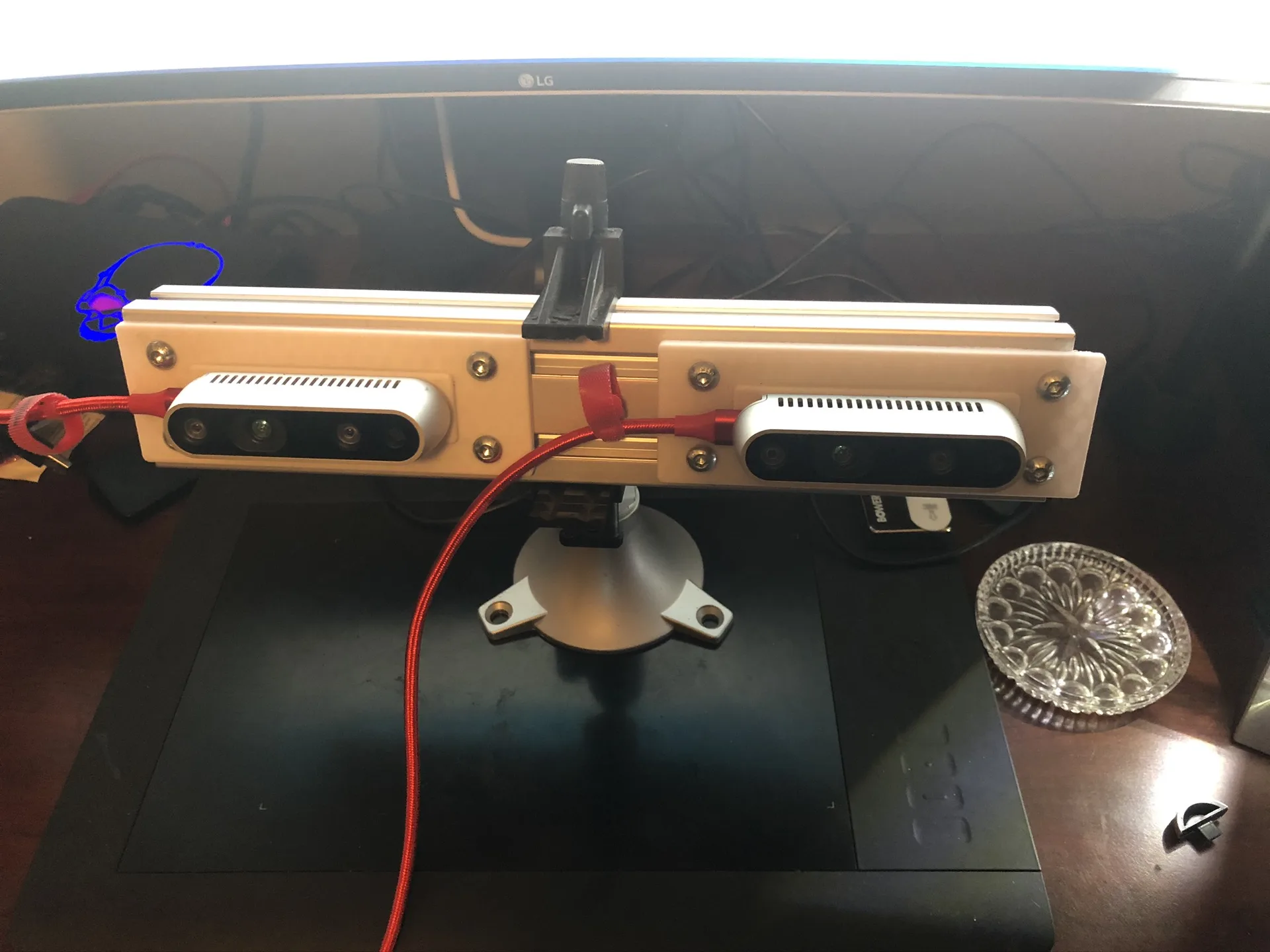 A narrow version of the rig, with two RealSense cameras on a light-colored printed bracket, clamped on top of a monitor.